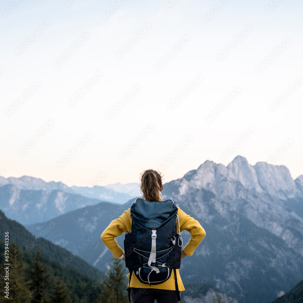 View from behind of a female hiker with backpack standing on top of a mountain looking at beautiful view