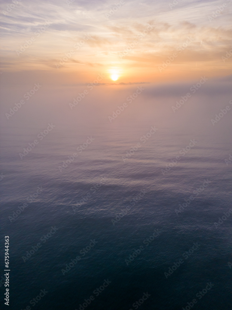 Aerial view of a sunrise sea with a blanket of morning fog and morning sunbeams shining through Aerial view of a sunrise sea with a blanket of morning fog and morning sunbeams shining through