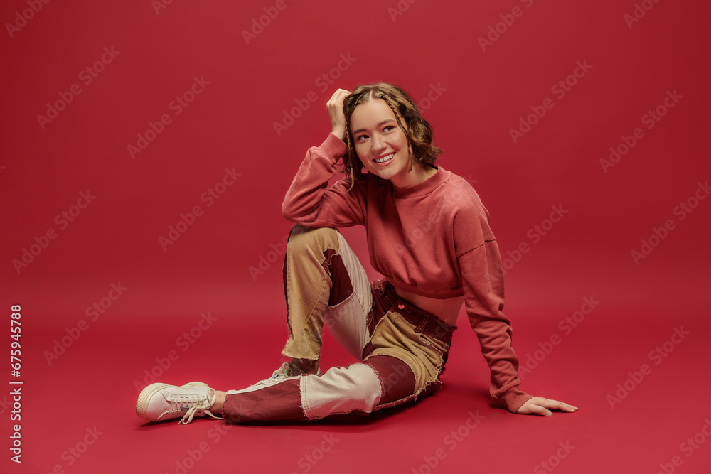 self-expression, cheerful woman in patchwork pants and cropped long sleeve sitting on red backdrop