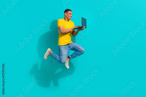 Full body profile portrait of active overjoyed young man jump run use netbook isolated on turquoise color background