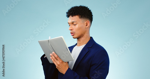 Man in studio, writing in notebook for ideas and business research for creative startup schedule. Thinking, agenda and young professional businessman with notes, pen and to do list on blue background