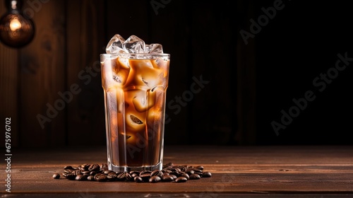 Ice coffee in a tall glass with cream poured over and coffee beans on a old rustic wooden table. Cold summer drink on a dark wooden background with copy space.