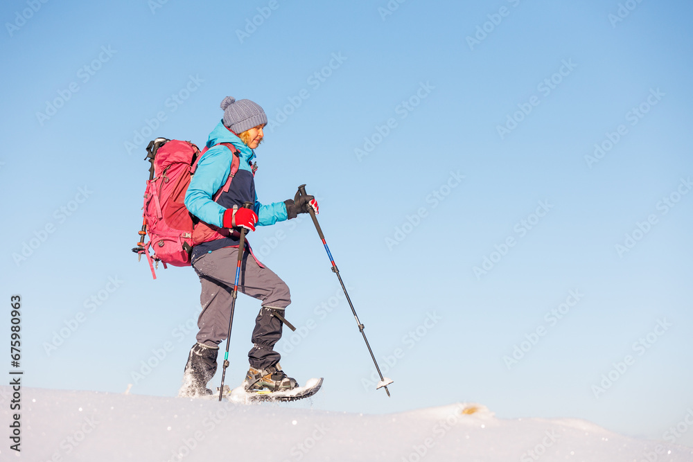 Fototapeta premium Climber in the mountains. A girl with a backpack and snowshoes walks through the snow.