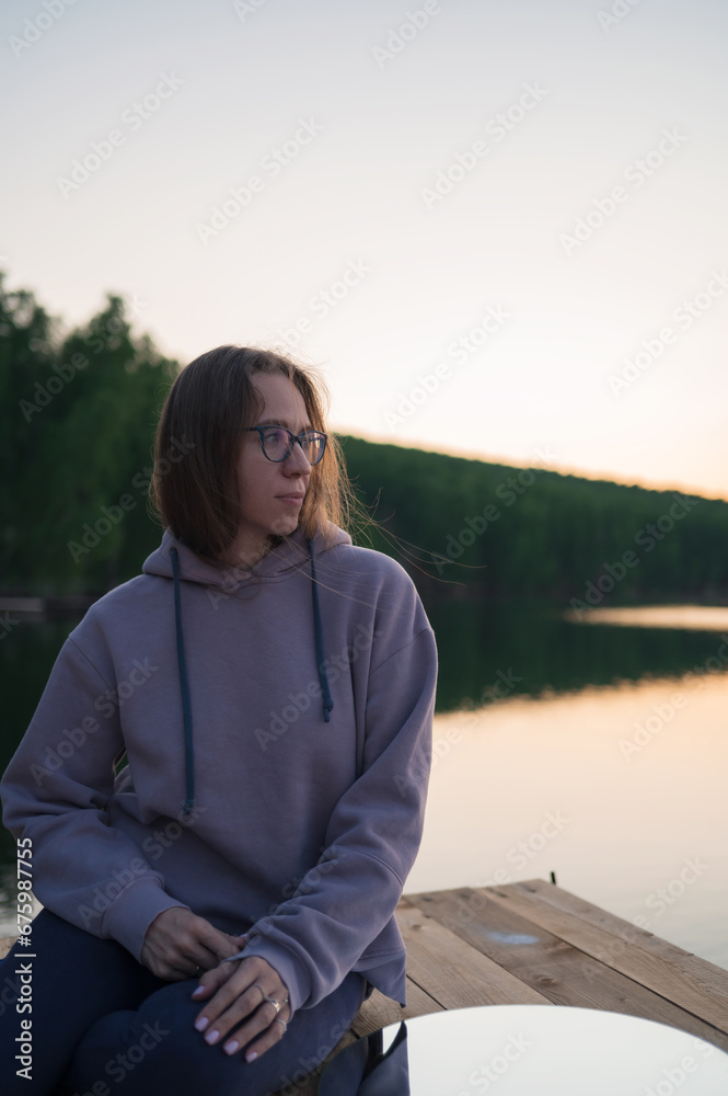 Woman sitting on the pier at lake with circle mirror, summer sunset