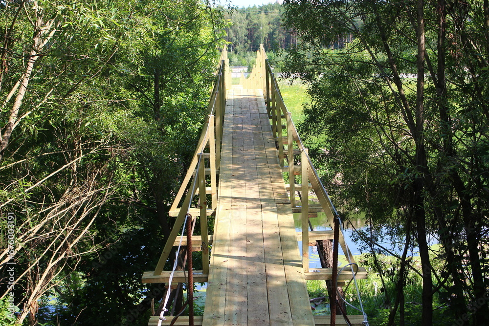 Obraz premium New wooden suspension bridge over the river for pedestrians in the countryside