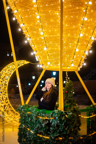 Beautiful woman in warm clothes, a hat and a coat in winter against the background of Christmas street lights. Celebrates the New Year on the street against the backdrop of street decor. bokeh