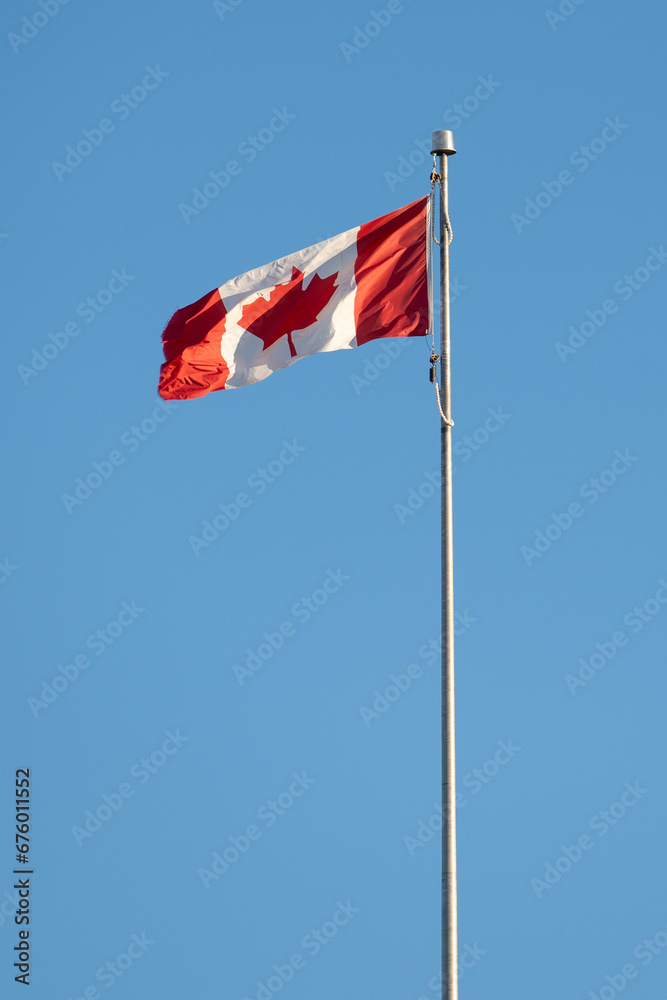 Canadian flag on pole in the wind with blue sky Canadian flag on pole in the wind with blue sky