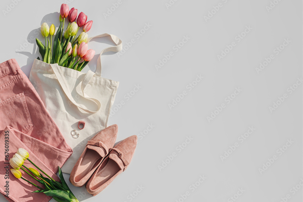 Fashion spring outfit. Pale pink jeans with bouquet of tulips flowers in bag,  and loafers. Women's stylish and elegant clothes with accessory and jewelry.  Flat lay, top view, overhead. - obrazy, fototapety, plakaty 