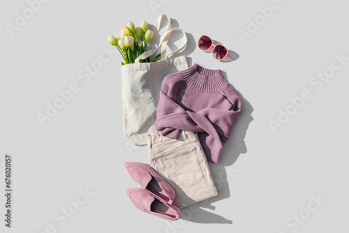 Fashion spring outfit. Purple jumper with bouquet of tulips flowers in bag, jeans and loafers. Women's stylish and elegant clothes with accessory and jewelry. Flat lay, top view, overhead.