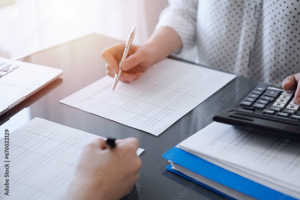 Two accountants use a calculator and laptop computer for counting taxes or revenue balance. Business, audit, and taxes concepts Two accountants use a calculator and laptop computer for counting taxes or revenue balance. Business, audit, and taxes concepts