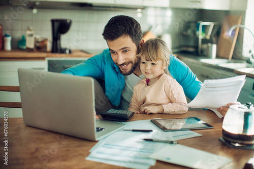 Young man holding document looking at laptop with daughter at home