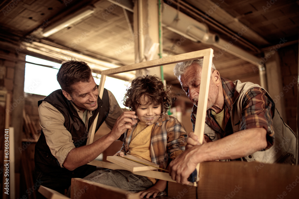 Adorable little boy learning carpentry from grandfather and father in workshop