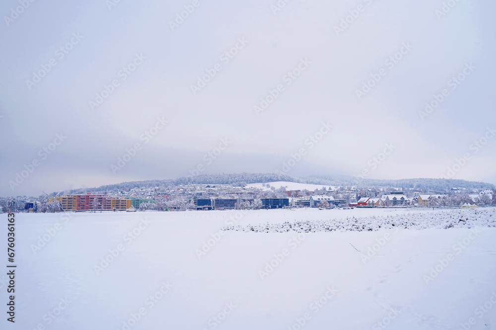 Panoramic view of village Urdorf in winter under extreme snow fall in January 2021. Residential quarter are on mild slope with forest behind it. 