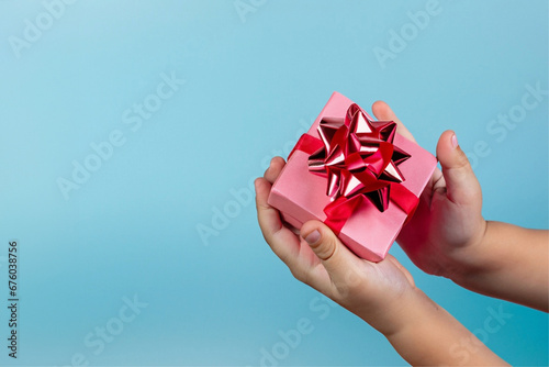 Mãos de uma criança segurando um presente com embalagem cor-de-rosa em um fundo azul claro. photo