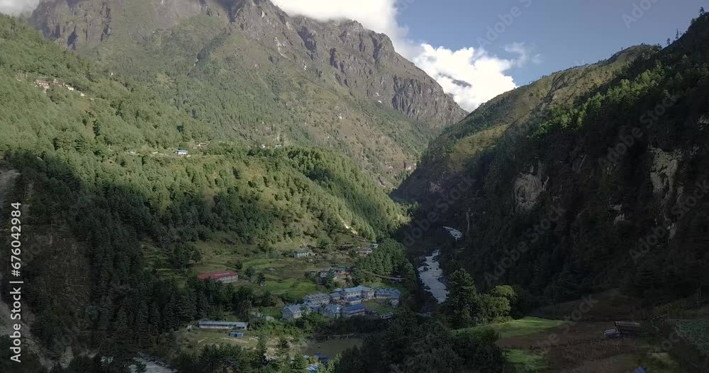 Shooting a mountain gorge in Nepal with snowy peaks and clouds with light fog during the day from a drone