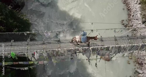 Donkeys loaded with belongings cross a suspension bridge over a river in Nepal