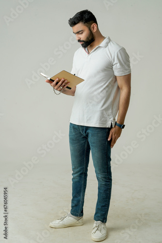 Young indian man standing with note book, isolated on white