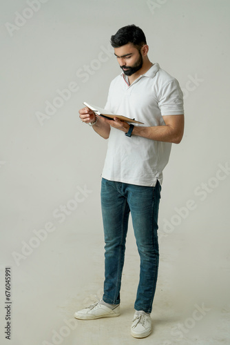 Young indian man standing with note book, isolated on white
