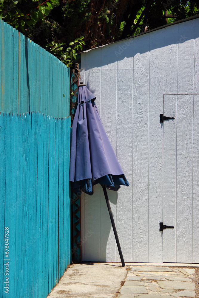 A closed purple parasol umbrella leaning against a turquoise fence A closed purple parasol umbrella leaning against a turquoise fence