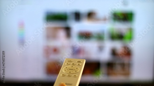 Fotografi mando a distancia blanco con television  de fondo mostrando la programacion de la tele a la carta
