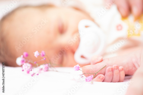 Limited focus sprig of delicate gypsophila flower with baby sleeping in background and holding mother's finger.