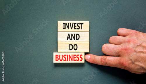 Invest and do business symbol. Concept word Invest and do business on beautiful wooden block. Beautiful grey table grey background. Businessman hand. Invest and do business concept. Copy space.