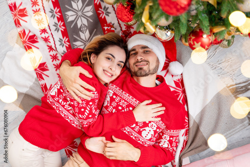 happy family a guy with a girl in red sweaters under the Christmas tree at home celebrate or wait for the New Year or Christmas rejoicing and hugging