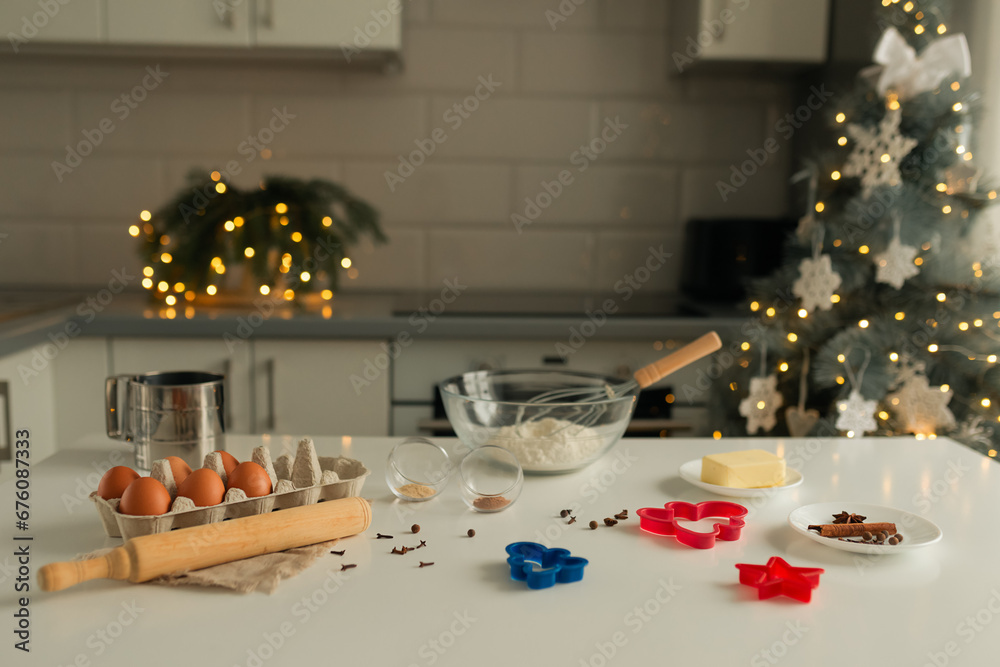 On the kitchen table there is a bowl with flour, a whisk, spices and molds for making Christmas cookies