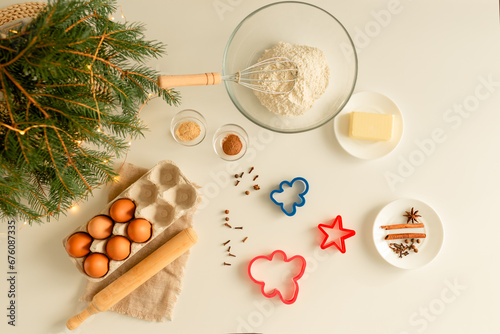 On the kitchen table there is a bowl with flour, a whisk, spices and molds for making Christmas cookies, top view