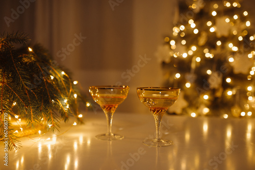 Two glasses of champagne are on the New Year's table. Christmas tree with garlands