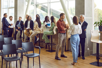 Full length photo of a group of diverse business people men and women chatting after meeting. Company employees or group of staff talking in modern office or conference room discussing work project.
