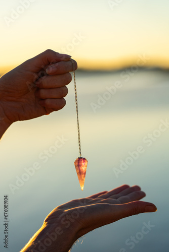 Woman's hands holding a pendulum with a lake behind