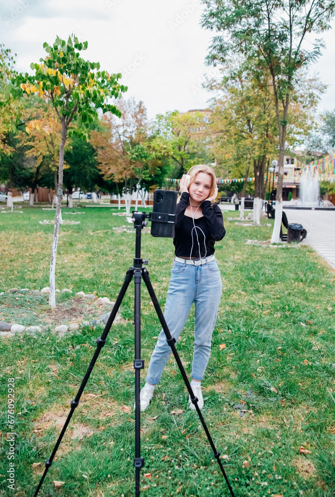 A teenage blogger girl shoots videos, records content. A blogger records a video on a mobile phone . A young girl is photographed in the park. An active lifestyle.