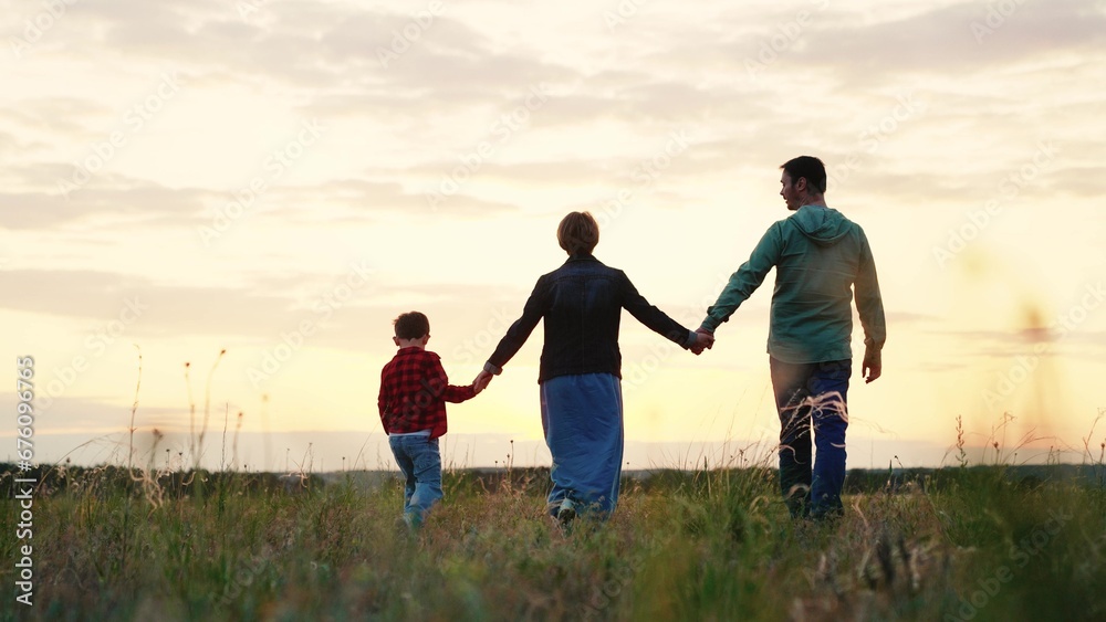 Happy family walks across grassy valley enjoying landscape view at sunset