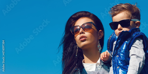 Portrait of fashionable baby boy and his gorgeous mother (hollywood star) in trendy sunglasses walking in the street. Sunny spring day. Close up. Copy-space. Outdoor shot