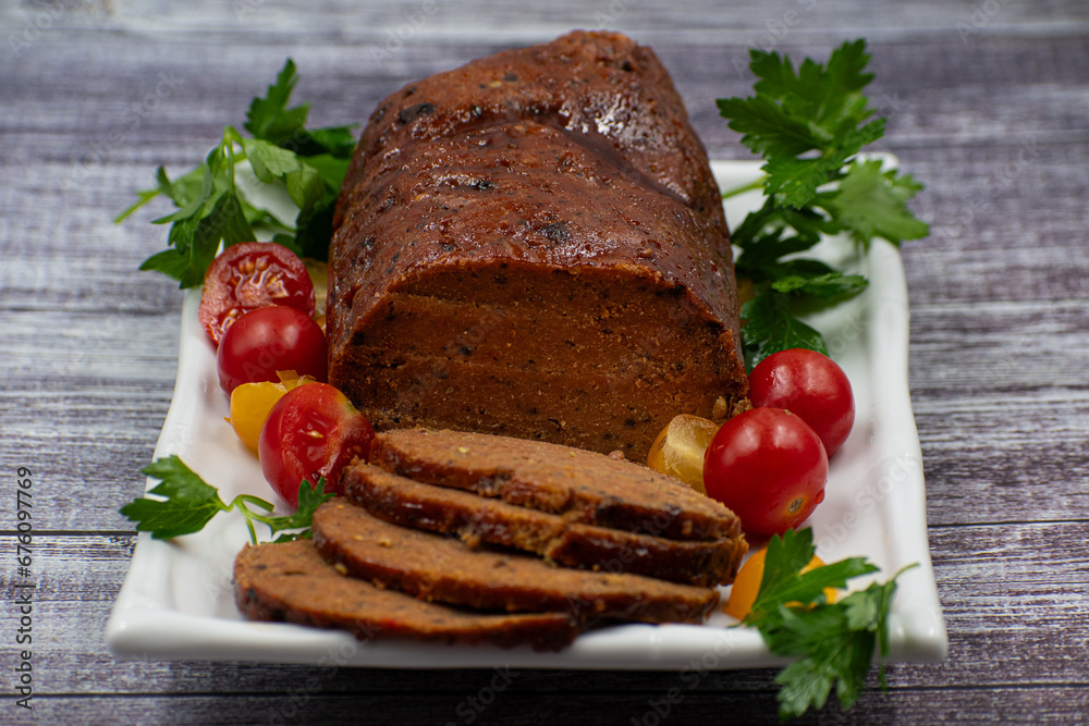 Vegan meat alternative- seitan seasoned with spiced, glazed with BBQ sauce. White plate, sliced, wooden table. Vegan meat alternative- seitan seasoned with spiced, glazed with BBQ sauce. White plate, sliced, wooden table.
