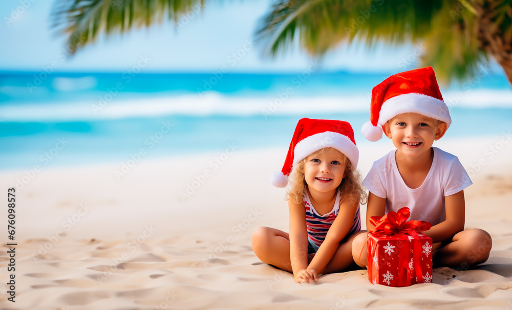 Obraz premium Children wearing Santa hats and holding Christmas presents while sitting in the sand on a tropical paradise beach. Shallow field of view.