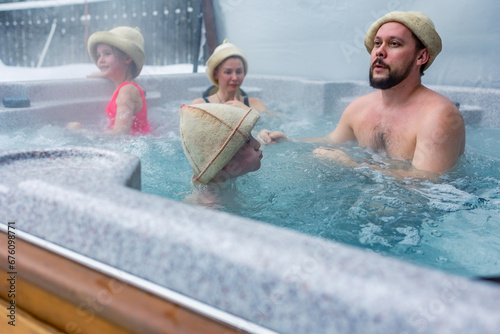 Cheerful happy family with children enjoys hot bath in jacuzzi whirlpool on cold winter day. Carefree relaxation in hot tub outdoors of nature. Meeting and chatting with relatives.