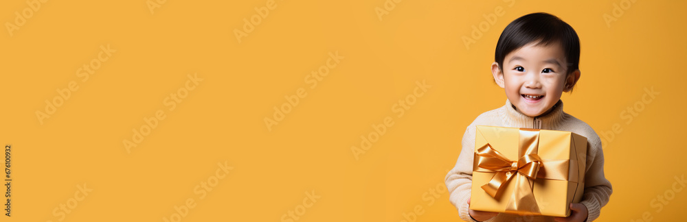 Baby with surprise package. Copy paste, horizontal. Present advertisement concept. Banner of young friendly smiling welcoming Asian toddler boy holding present box with bow, orange studio background Baby with surprise package. Copy paste, horizontal. Present advertisement concept. Banner of young friendly smiling welcoming Asian toddler boy holding present box with bow, orange studio background