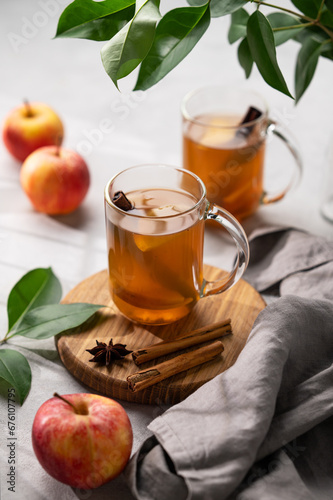 Homemade apple cider with apples and cinnamon in cups on a wooden board on a light background with fresh fruits, spices and branch.