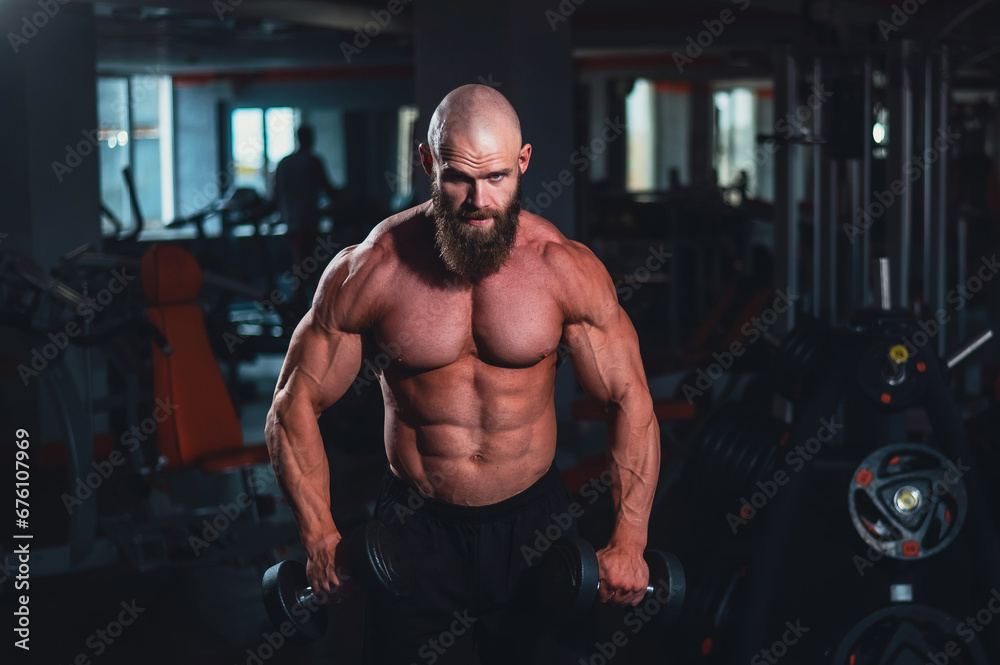 A muscular shirtless man lifts dumbbells to the sides with dumbbells in the gym.