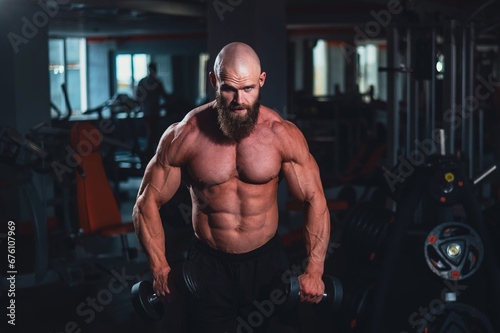 A muscular shirtless man lifts dumbbells to the sides with dumbbells in the gym.