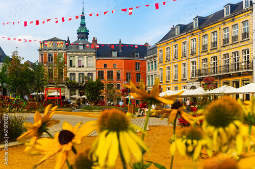 Picturesque summer view of flowering central Grand Place square in Mons overlooking baroque belfry of Roman Catholic Church of St. Elizabeth towering over colorful residential townhouses, Belgium