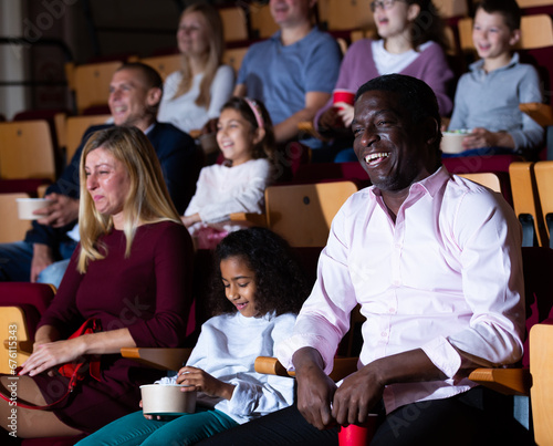 Happy international family eating popcorn and watching comedy in cinema hall