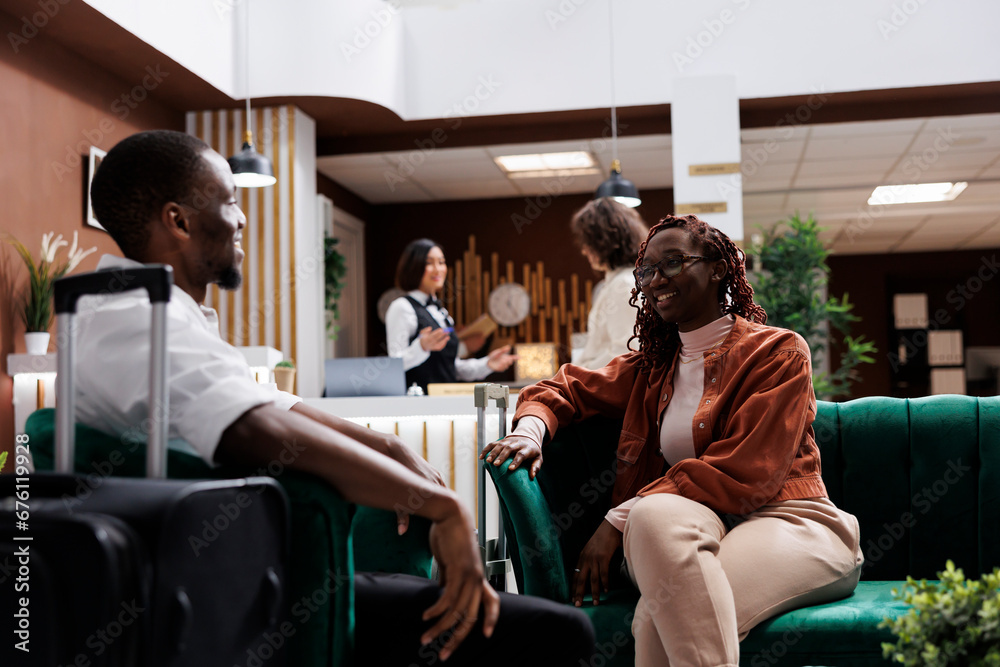 Young couple waiting to do check in at hotel reception, relaxing on couch in luxury lounge area. African american people sitting in modern resort lobby before filling in registration forms. Young couple waiting to do check in at hotel reception, relaxing on couch in luxury lounge area. African american people sitting in modern resort lobby before filling in registration forms.