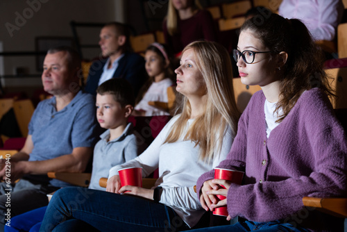Number of happy glad friendly people enjoying film screening and popcorn in cinema