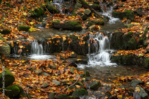 Flowing river with small waterfalls with leaves in autumn colors.