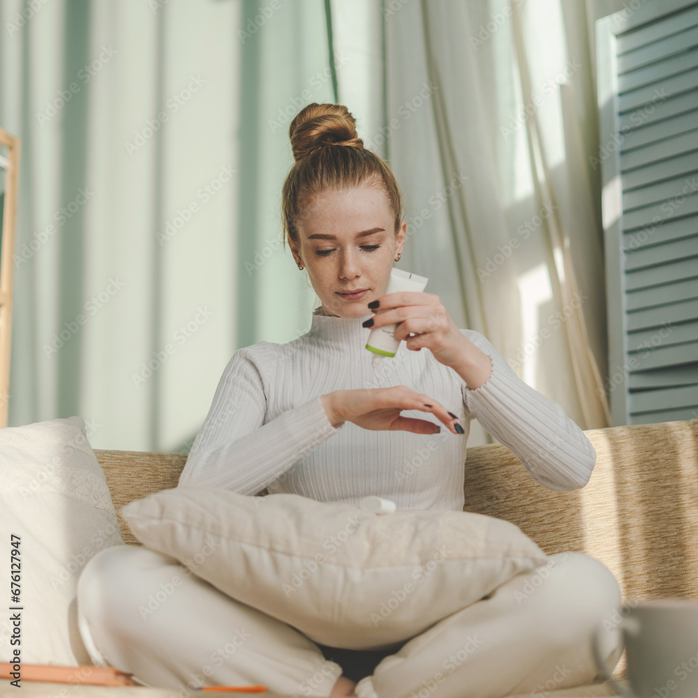Woman applying moisturizing cream on hand sitting on sofa, enjoying body skincare procedure with anti aging cosmetic product at home. Skincare routine concept Woman applying moisturizing cream on hand sitting on sofa, enjoying body skincare procedure with anti aging cosmetic product at home. Skincare routine concept