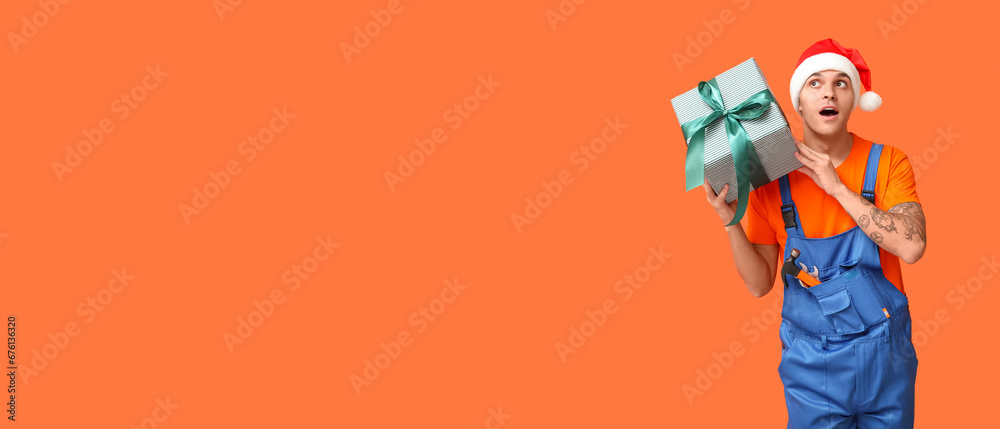 Repairman in Santa hat and with Christmas gift on orange background with space for text Repairman in Santa hat and with Christmas gift on orange background with space for text