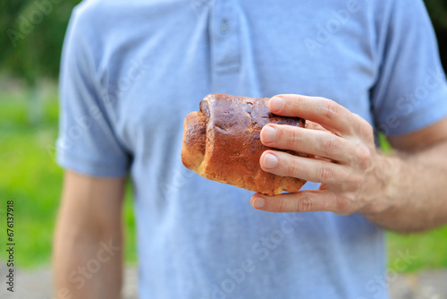 A man's hand holds a cinnamon pastry, snack and fast food concept. Selective focus on hands with blurred background